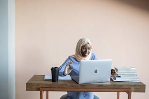 Smiling Muslim woman in hijab waving during an online video call.