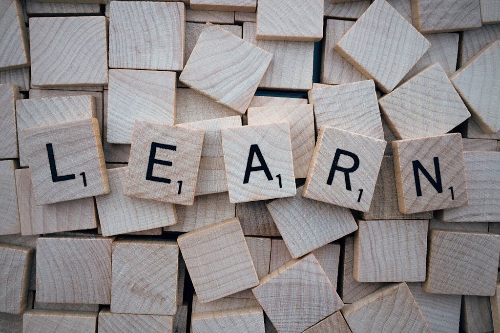 Wooden letter tiles arranged to spell 'learn' on a background of scattered tiles.